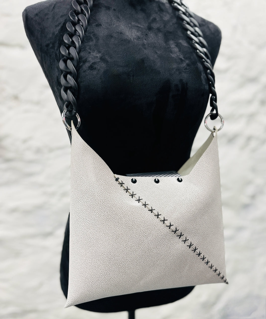 White handbag with black chain strap on a mannequin against a textured white background