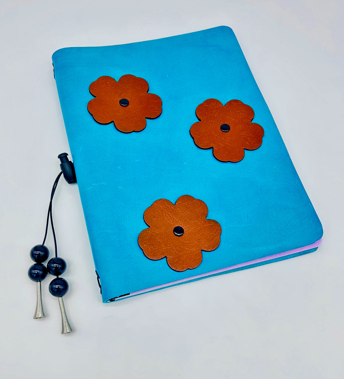 wide shot of a blue Leather Journal with embossed brown leather flowers and a beaded tassel