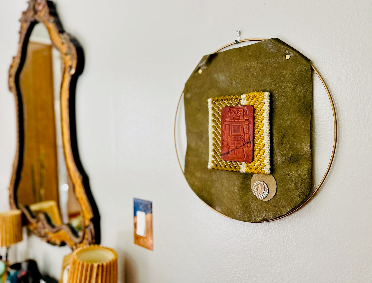 Decorative wall art with geometric design on a green background, mirror and light switch visible in the background.