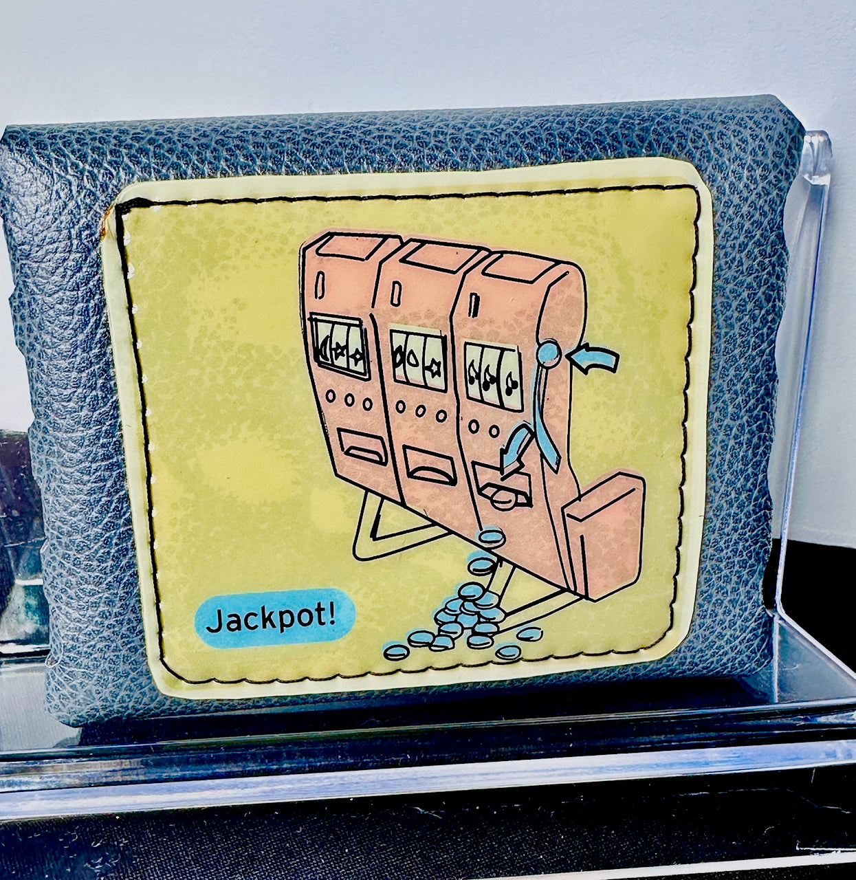 Blue wallet with a slot jackpot machine illustration and 'Jackpot!' text on a clear stand.