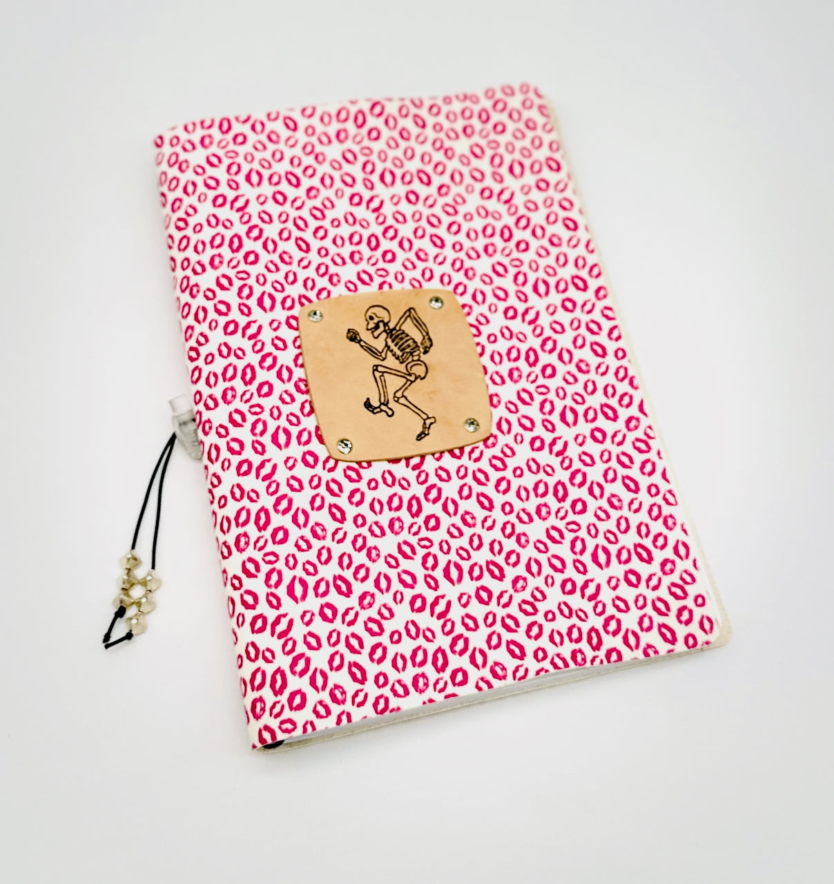 Front cover of leather journal featuring a dancing skeleton on a background of pink lipstick kisses
