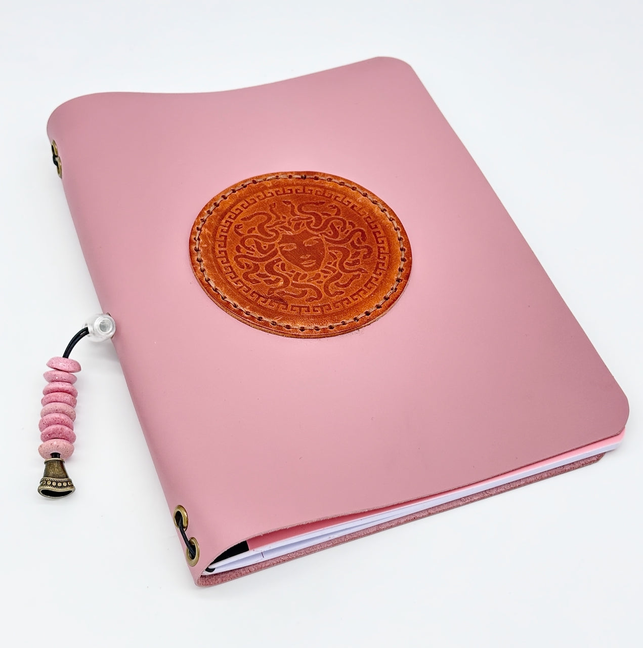 Front cover of pink leather journal with medusa medallion and pink beaded tassle