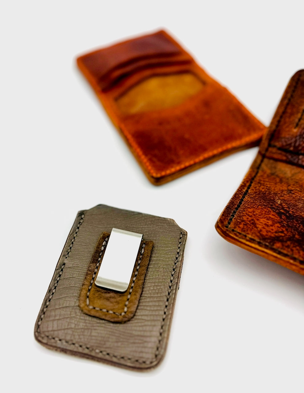 Two leather wallets, one brown and one gray with a metal clip, on a white background.
