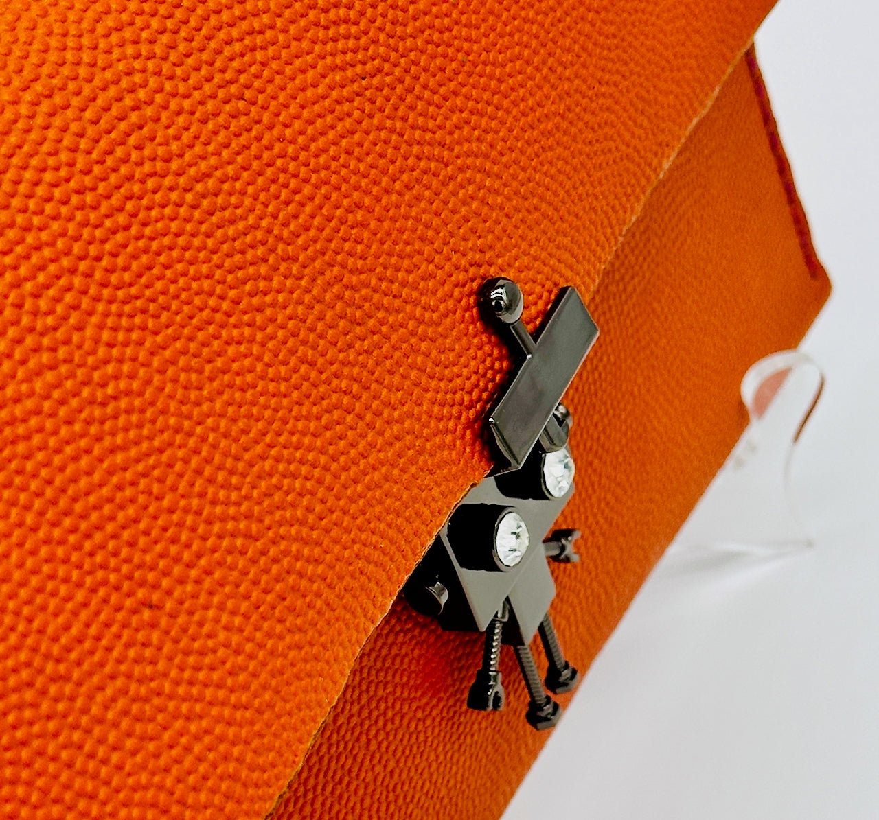 Metallic robot clasp latch with a small robot design attached to an orange textured leather clutch purse.
