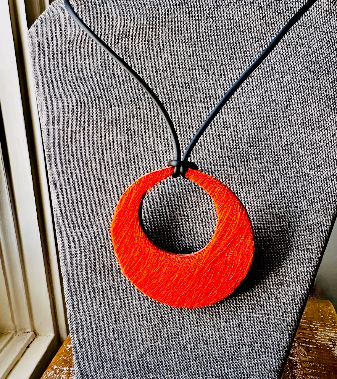 Orange circular hair on hide leather circular pendant on a black cord against a gray fabric background