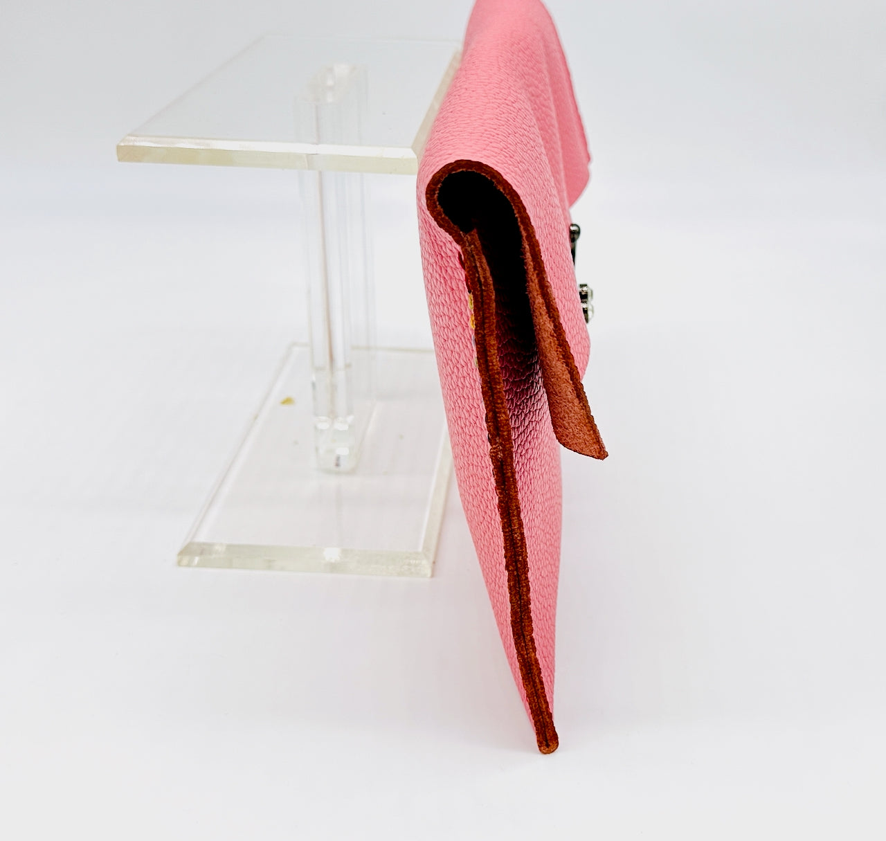 Pink clutch bag profile on a clear stand against a white background