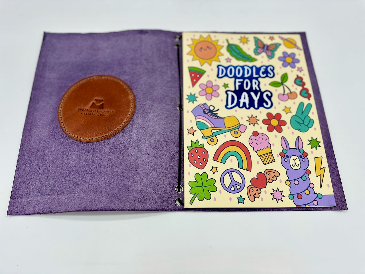 Purple notebook with a brown leather patch and colorful doodles on the cover.