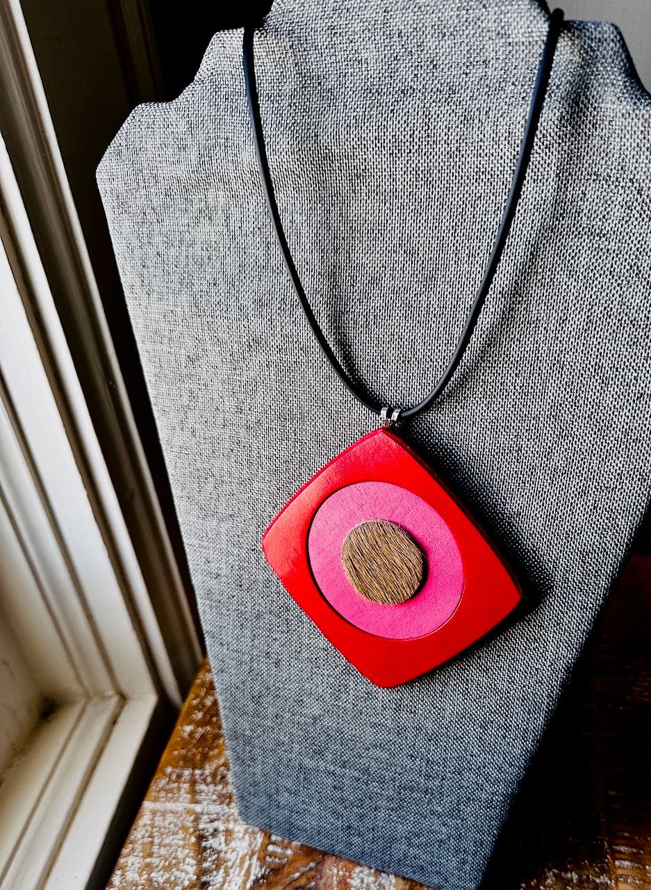 Necklace with a red and pink leather pendant on a gray fabric easel.