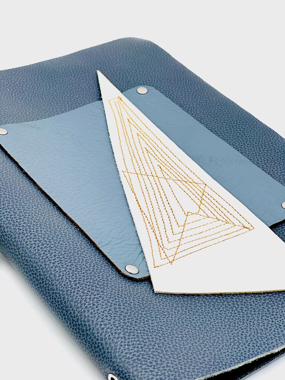 Blue leather blank journal with a white triangle of leather featuring gold geometric design on a light gray background