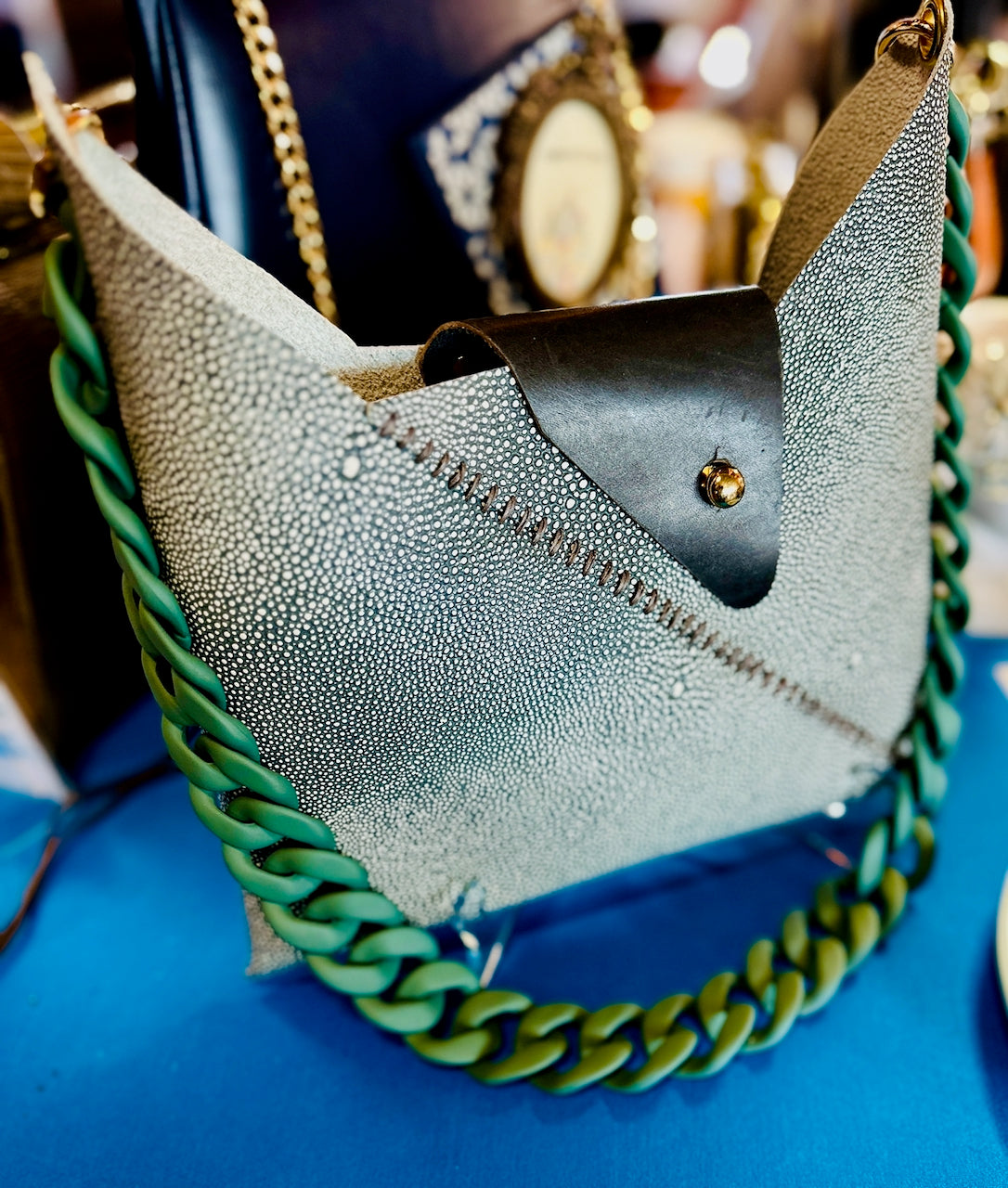 Shagreen leather crossbody handbag with green chain strap handle on a blue surface
