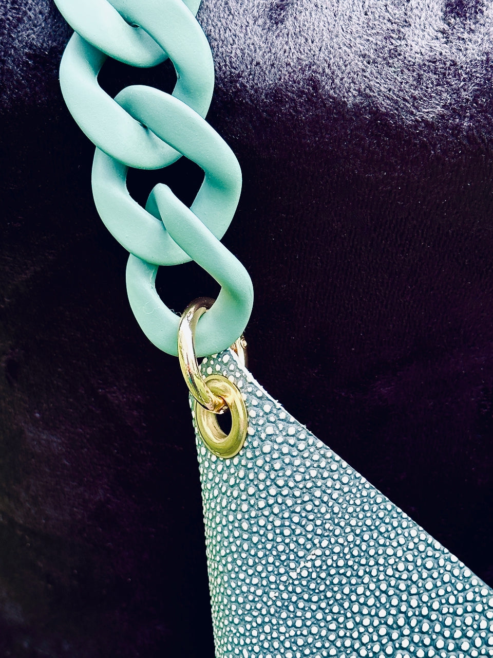 Close-up of a turquoise chain handle attached to a textured teal bag against a dark background