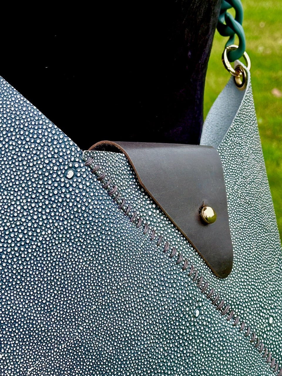 Close-up of a textured green shagreen leather crossbody handbag with a leather patch and green chain strap.