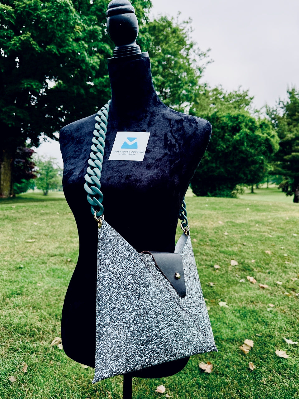 Greenish leather shagreen handbag with a pea green matte acrylic chain strap on a mannequin torso outdoors.