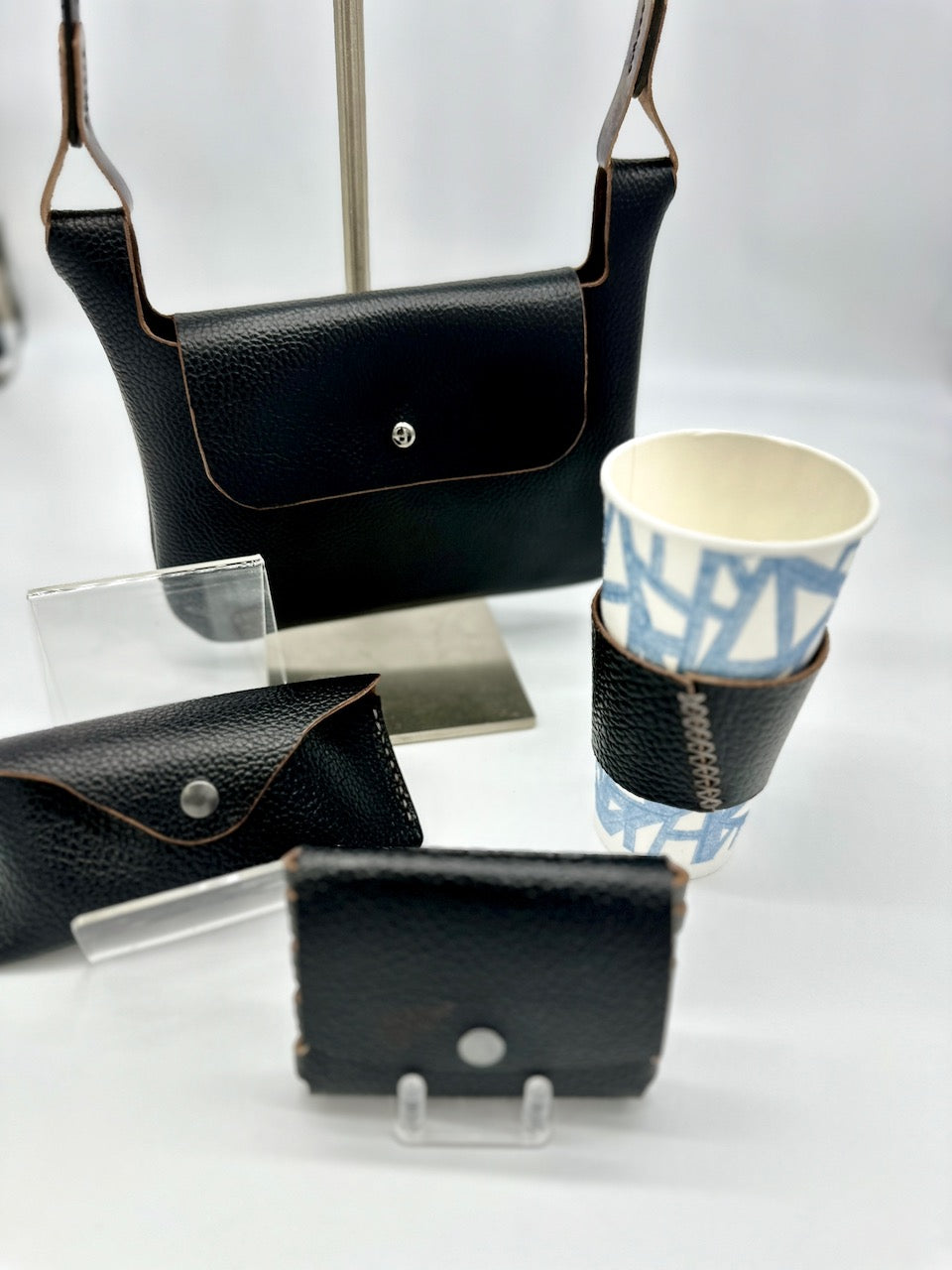 family of black leather products, including a glass case, wallet, coffee sleeve and purse