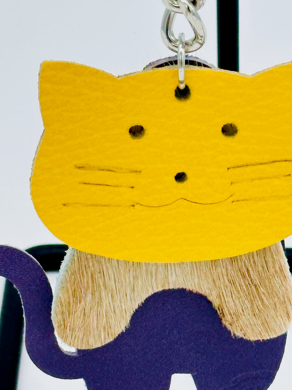 closeup of cat key chain and purse fob made of leather in colors of yellow, purple and tan