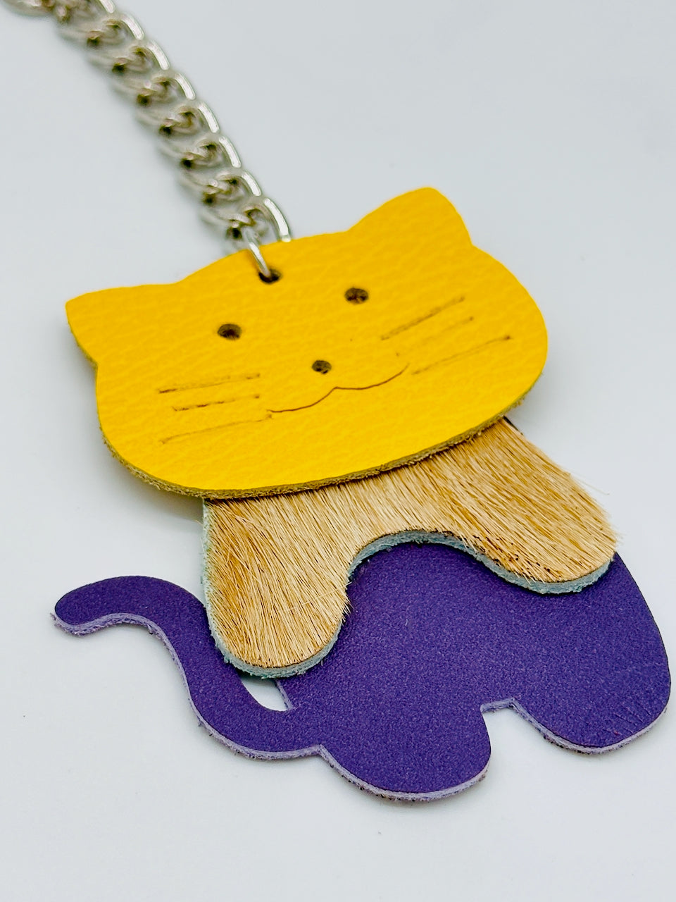 leather key chain in the shape of a three piece cat lays flat on table