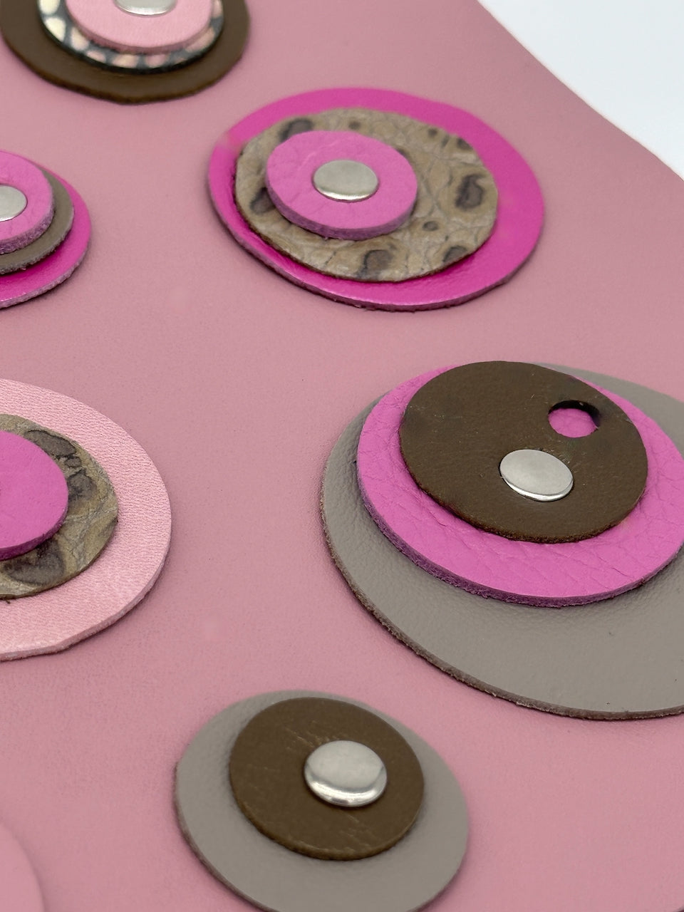 close up image of circles with rivets on front cover of pink leather journal.