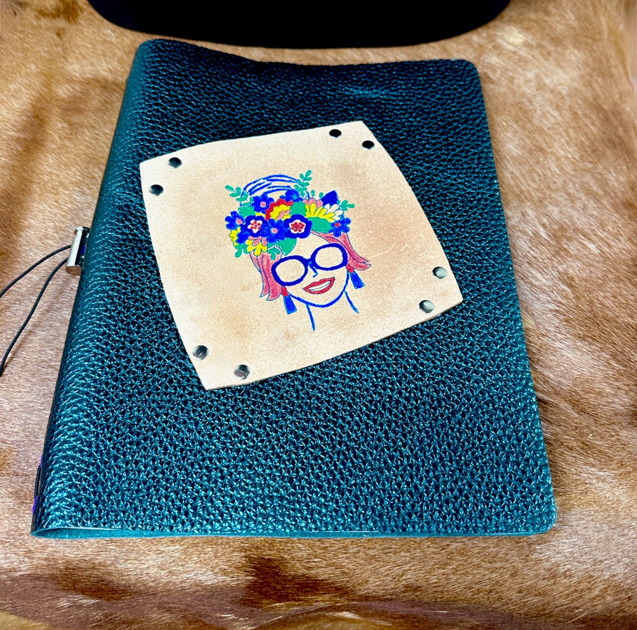 woman with sunglasses and a crown of flowers in her hair on the top of a green metallic leather refillable journal