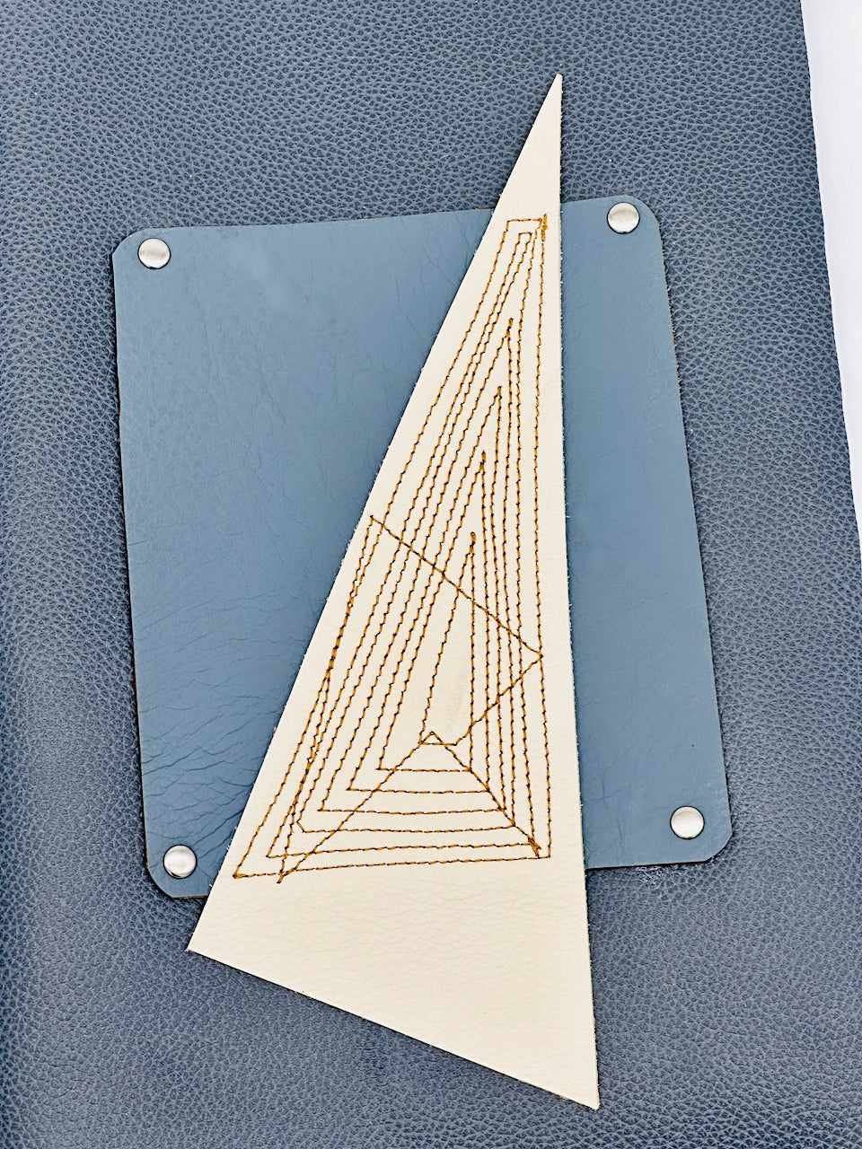 Triangle-shaped embroidered piece on a blue leather background