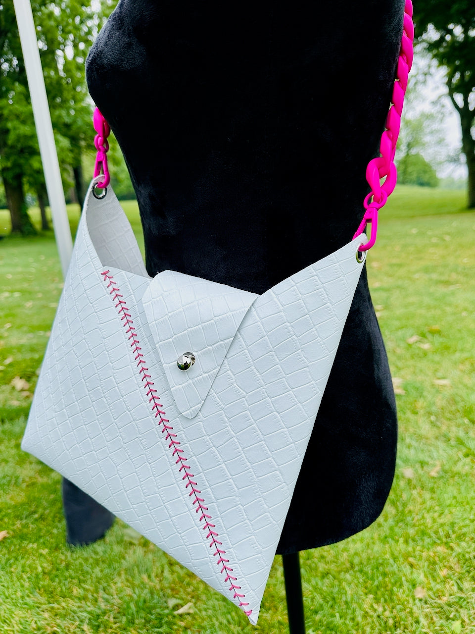 White crocodile embossed leather crossbody handbag with pink strap and pink stitching on a mannequin outdoors.