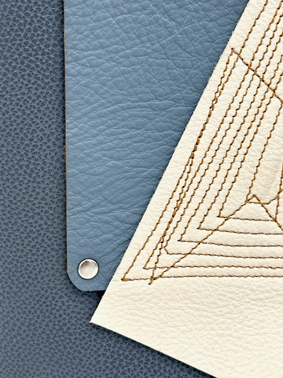 Close-up of blue leather and beige quilted fabric with stitching details.