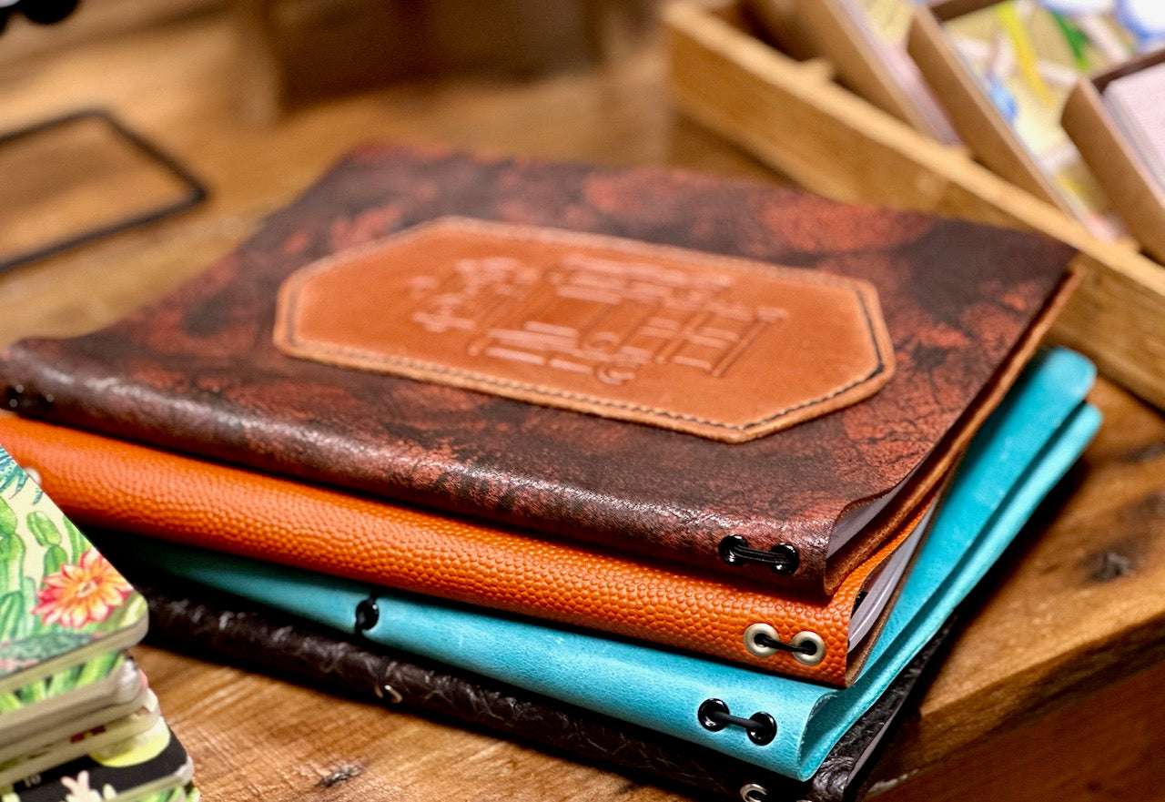 Robbie the robot leather journal sits atop three other leather refillable journals from Undercover Popular Leather Goods.