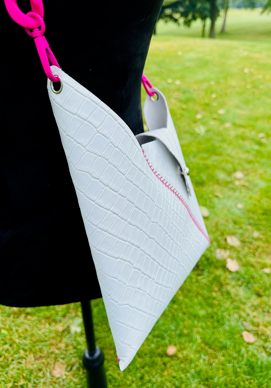 White reptile textured leather crossbody bag with pink strap on black velvet mannequin
