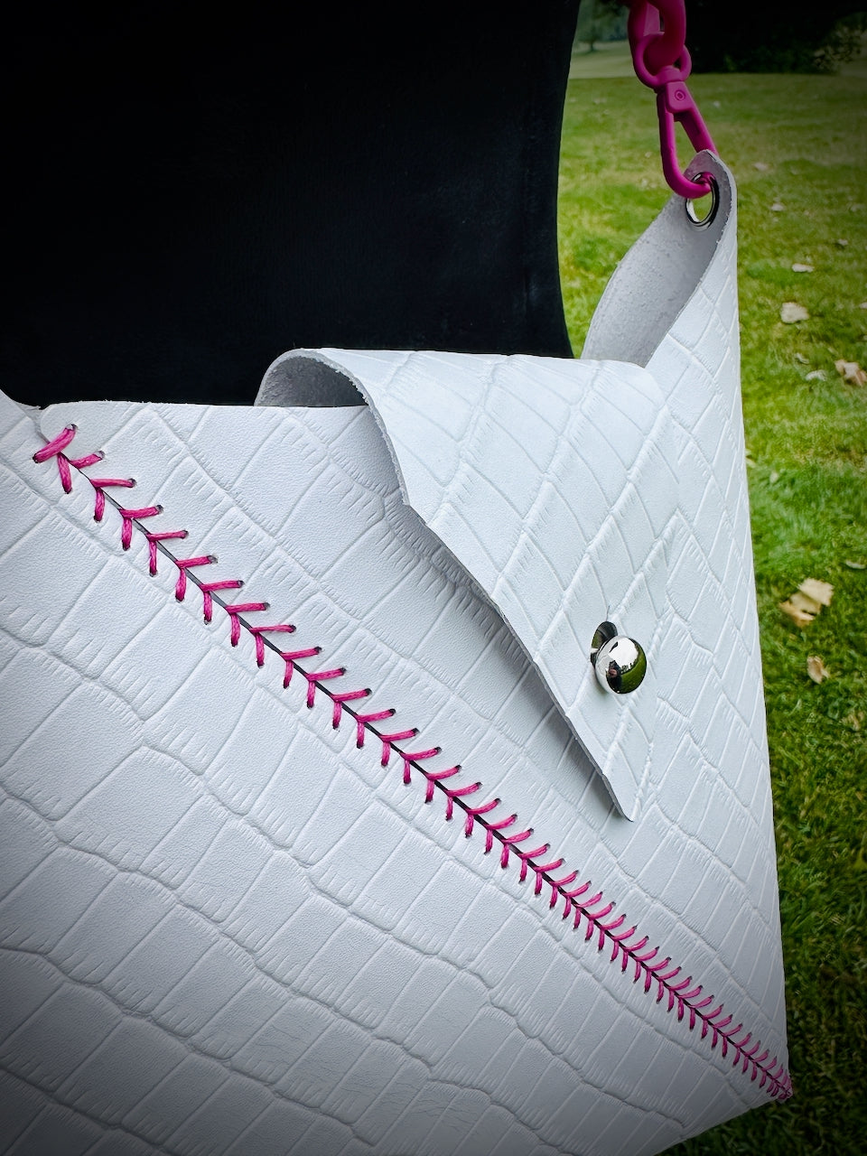 White crocodile embossed leather crossbody bag with pink stitching detail on a grassy background