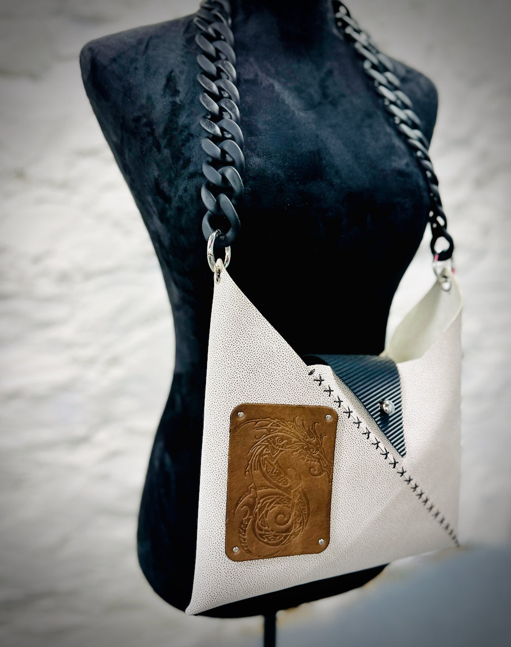 White handbag with green leather dragon patch on a mannequin against a neutral background
