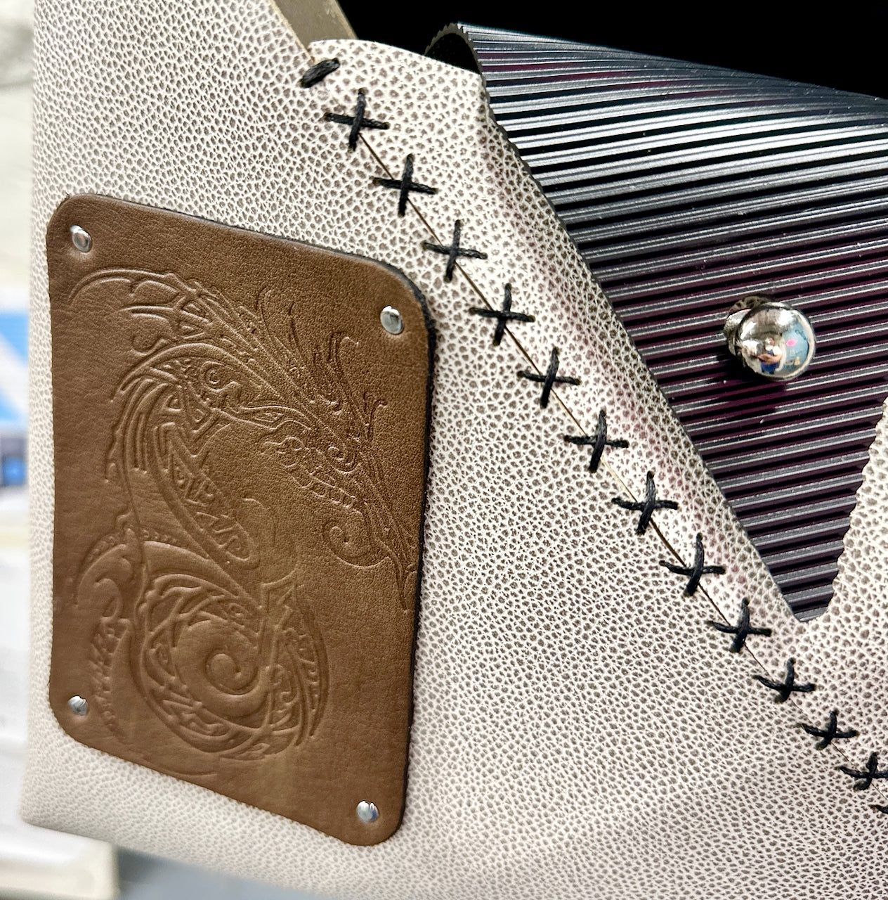 Close-up of a textured white purse with black stitching and a green leather patch with embossed dragon design.