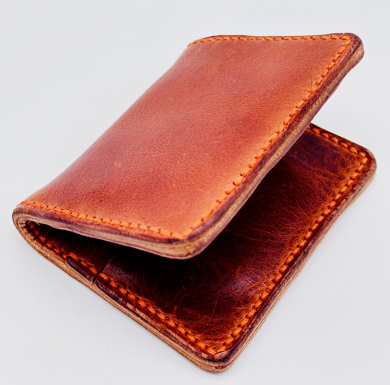 Cognac leather wallet with orange stitching on a light gray background