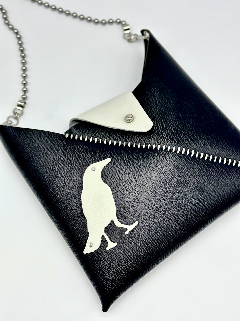 Black purse with white hand stitching and a white bird design on a white background
