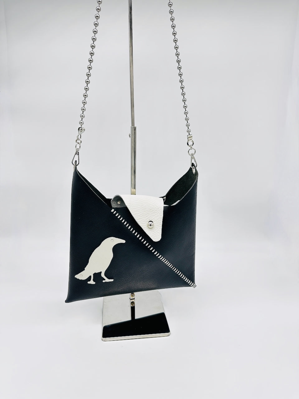 Black handbag with a white bird design on a stand against a white background