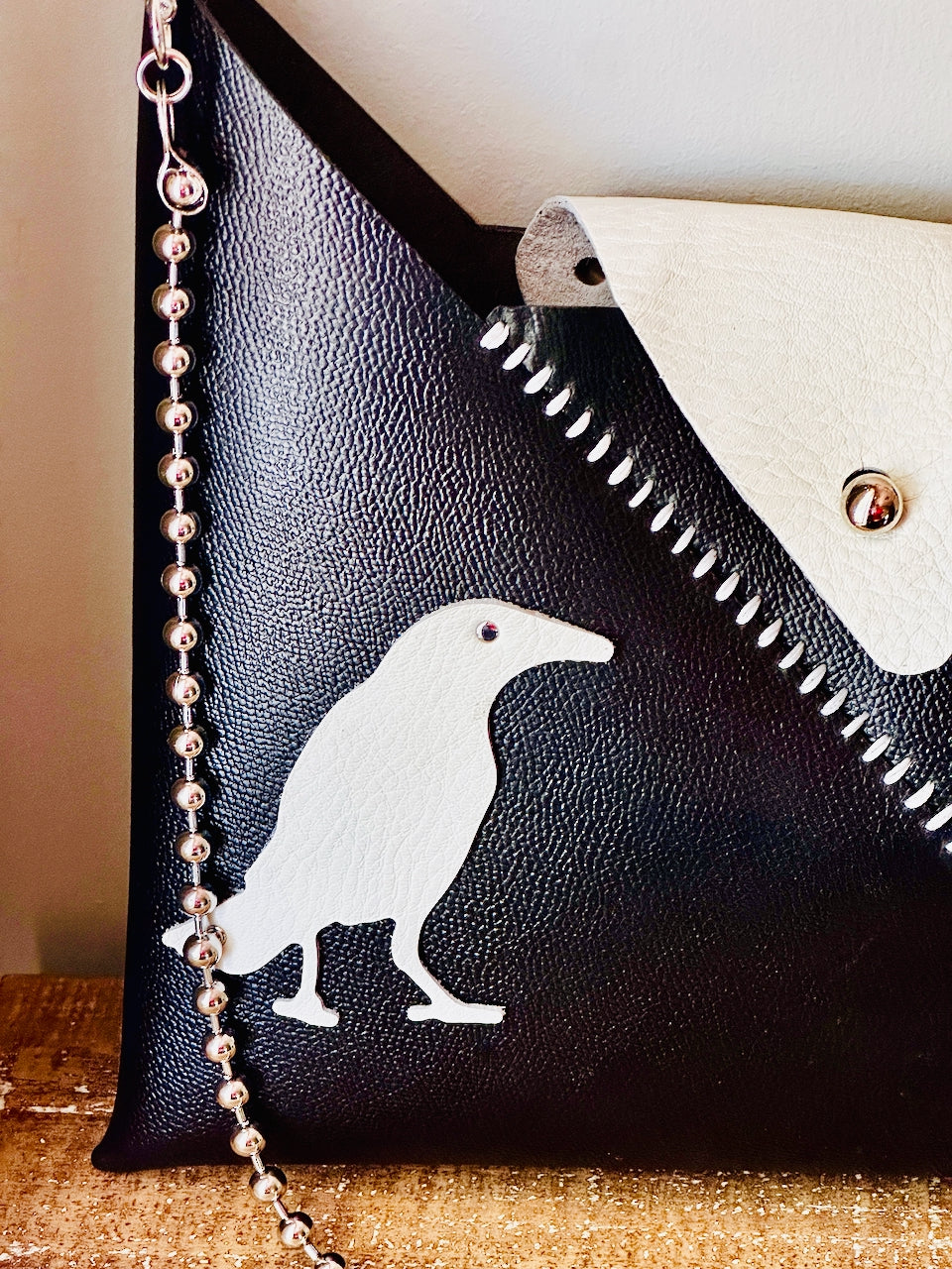 Black leather clutch with white bird design and chain strap on a wooden surface.