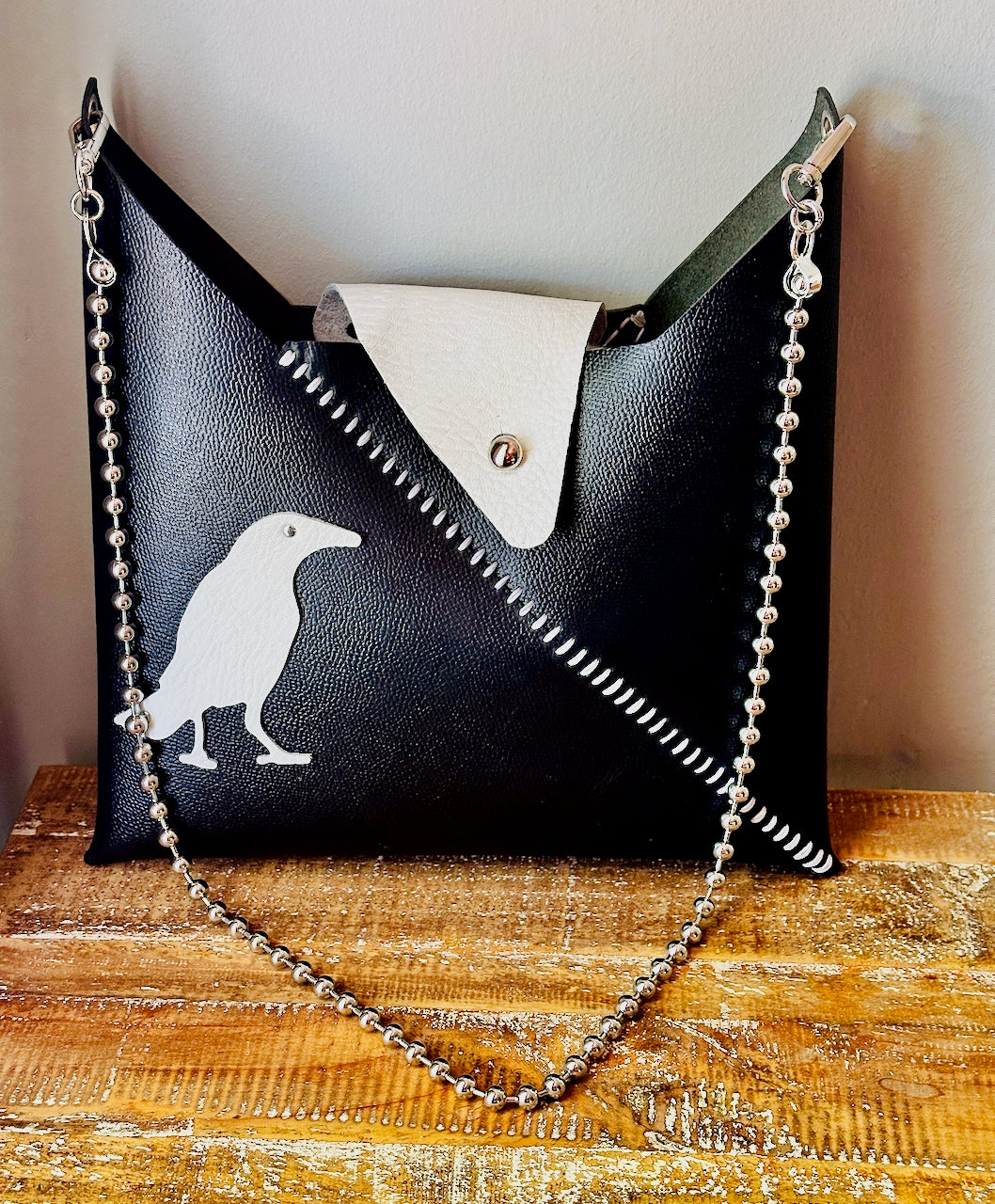 Black leather handbag with a chain detail on a wooden surface