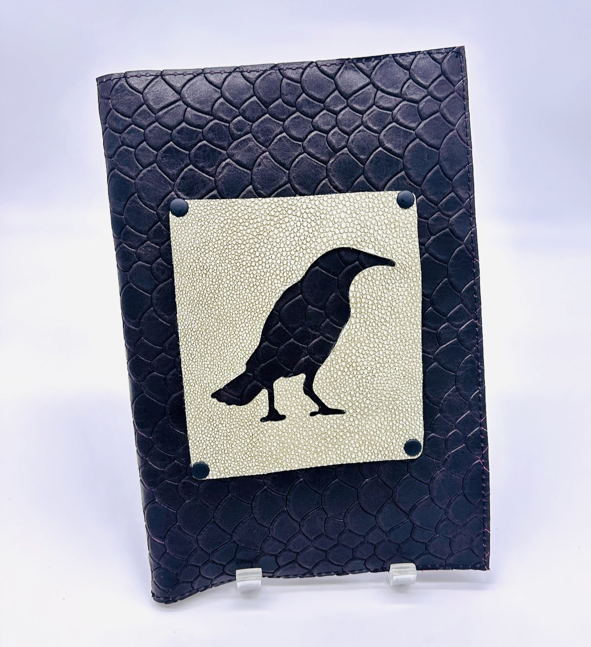 Black leather-bound book with a green shagreen leather square featuring a black crow silhouette on a light gray background