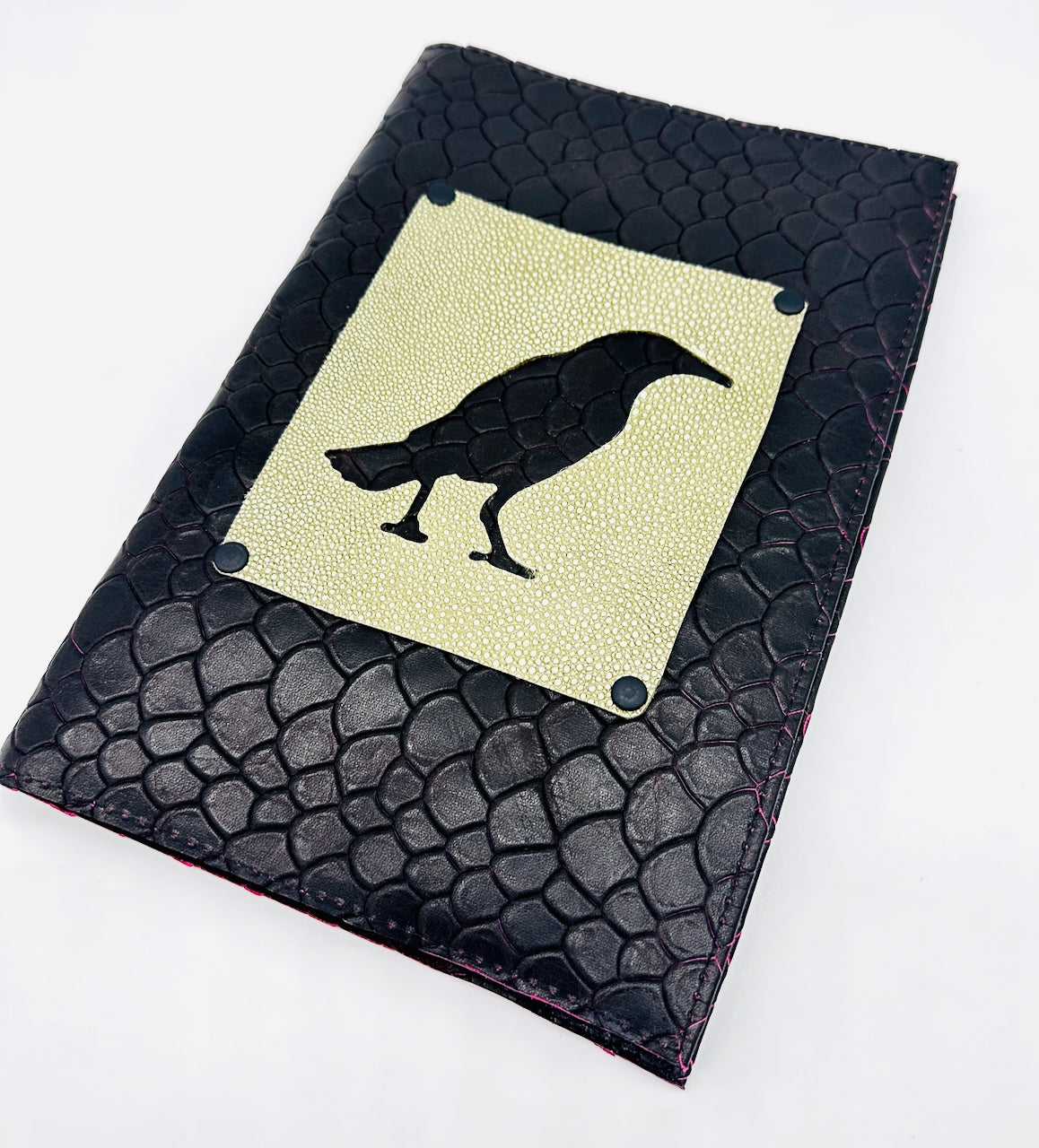 Black dragon scale textured leather notebook with a green embossed crow design on a white background