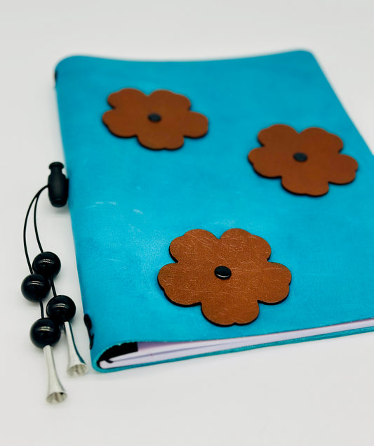 low angle view of a handmade blue leather journal cover with brown embossed leather flowers and rivets