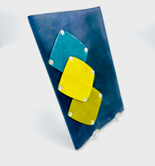Blue suede journal with geometric yellow, pea green and teal patches on a white background