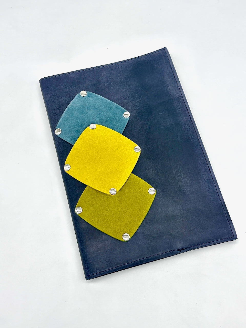 Blue refillable journal with yellow, green and teal geometric patches on a white background