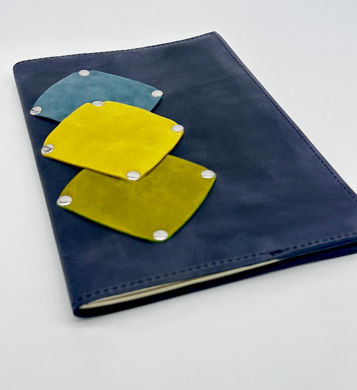 Blue journal notebook with yellow, green and teal patches on a white background
