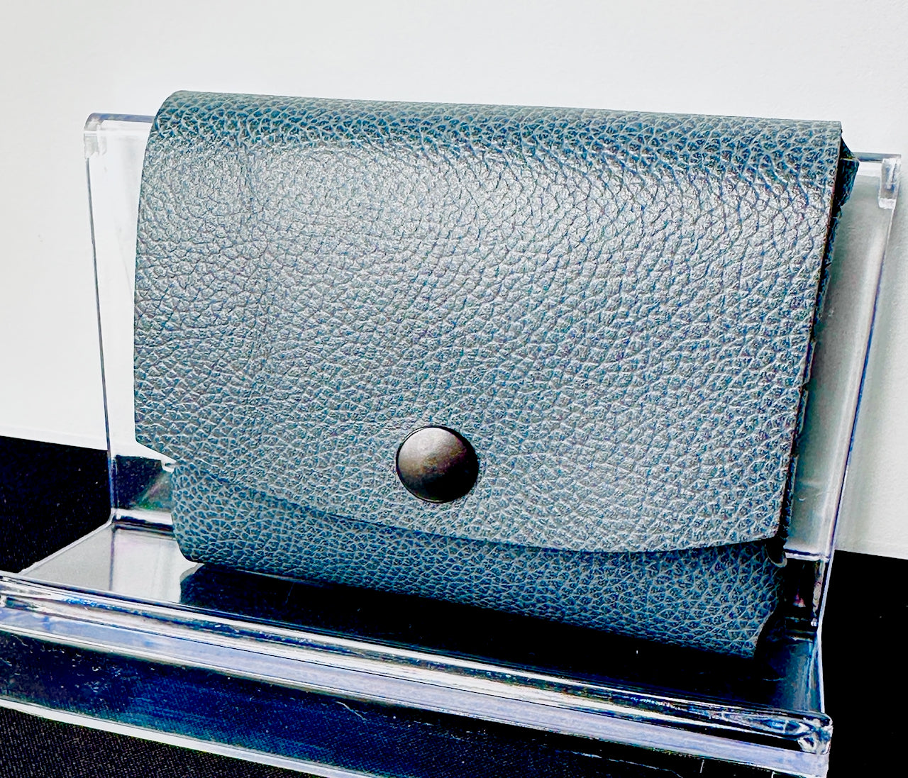 Blue textured leather wallet on a clear stand with a white background