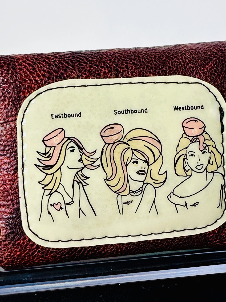 Leather wallet with a decorative patch featuring three women labeled 'Eastbound', 'Southbound', and 'Westbound'.