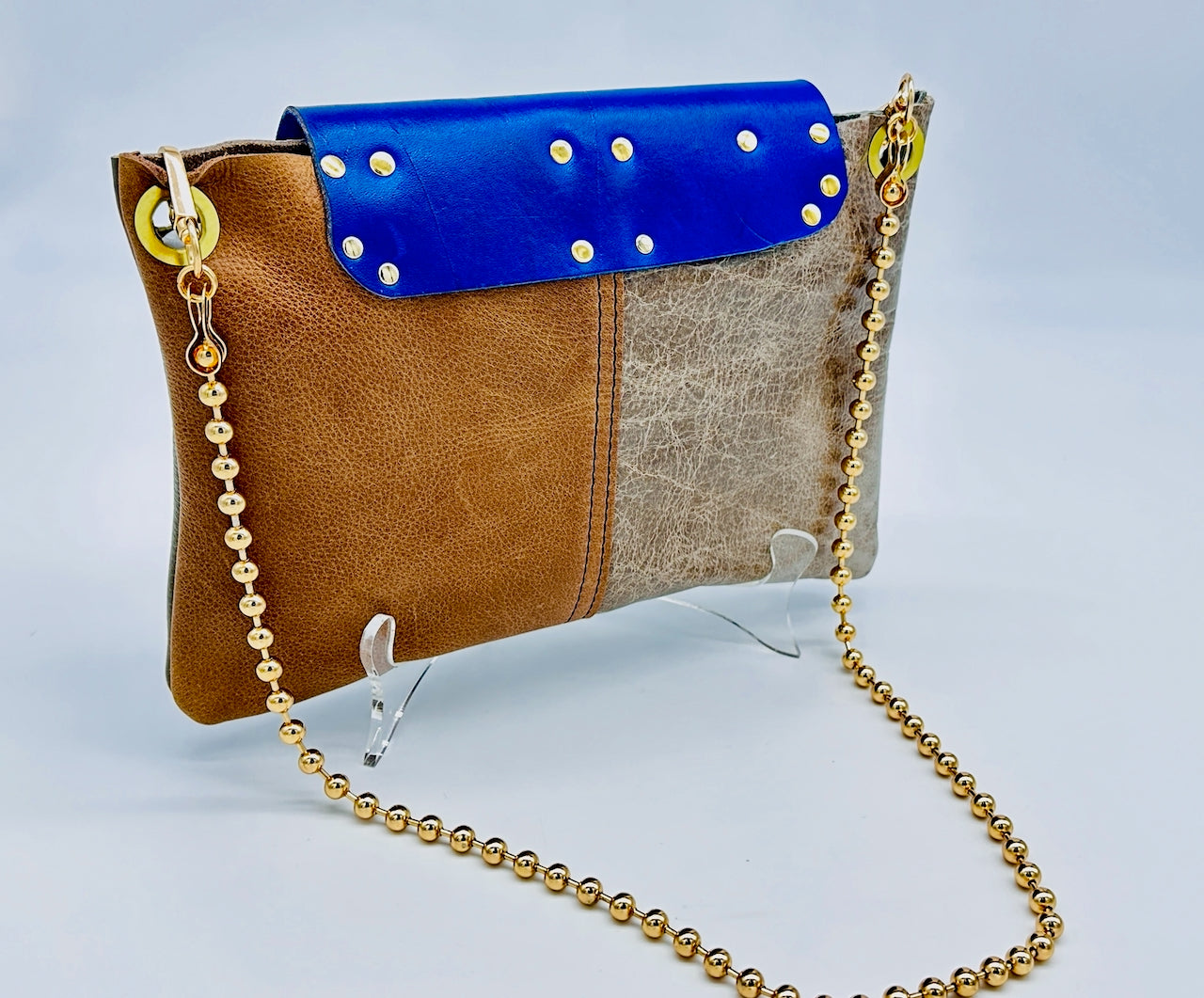 Back side of a multicolored handbag with a blue flap and gold chain strap.