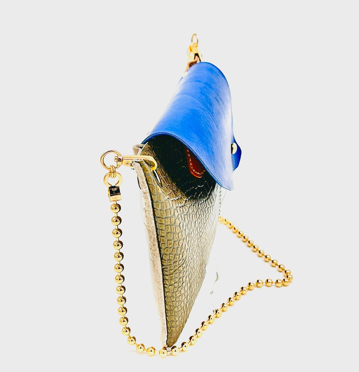 profile of a leather handbag with blue top and gold chain on a white background
