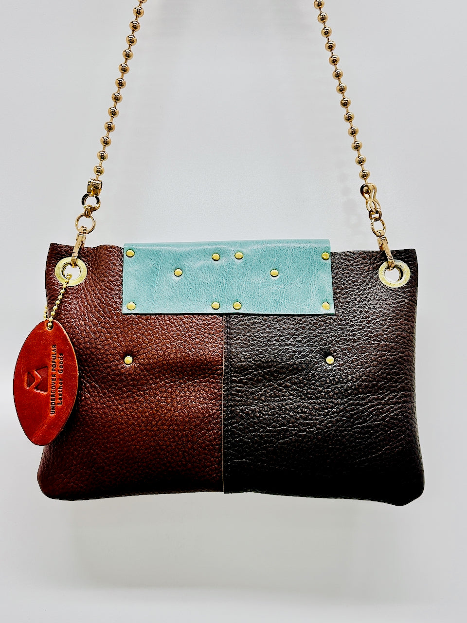 Back side of colorblock purse featuring, turquoise brown and dark brown leather with gold chain strap.
