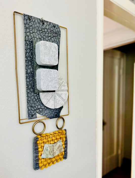 Decorative wall art with geometric shapes and a gold frame on a white wall.