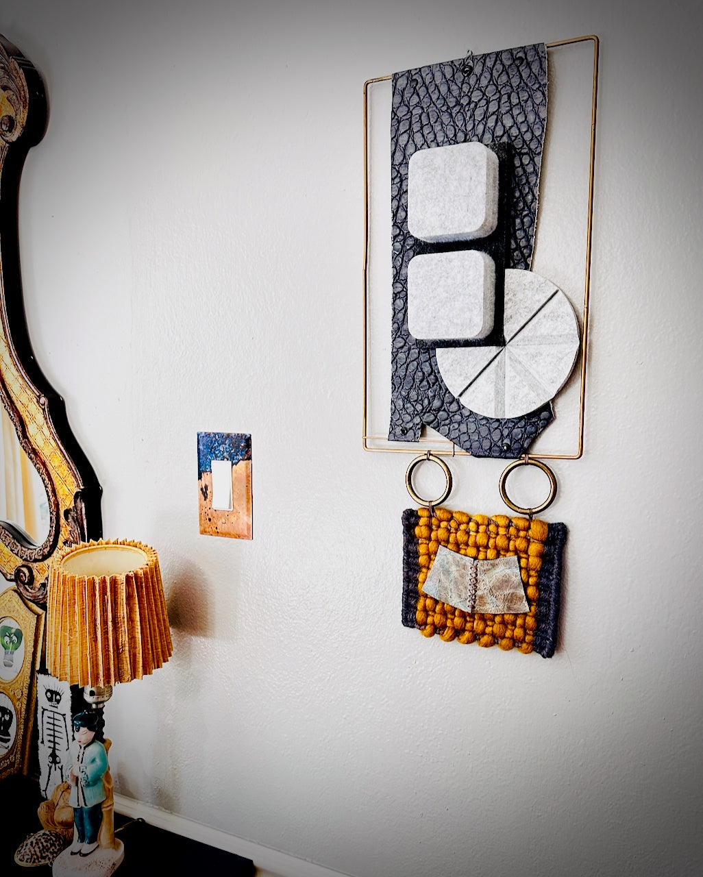 Decorative wall art with geometric design and a lamp on a white wall.