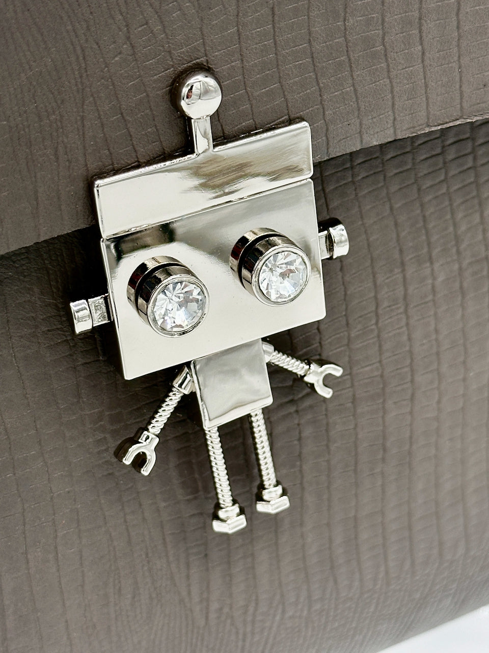 Metallic robot-shaped lock clasp on a textured leather purse