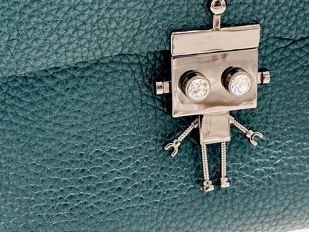 Silver robot-shaped clasp on a textured green leather purse 